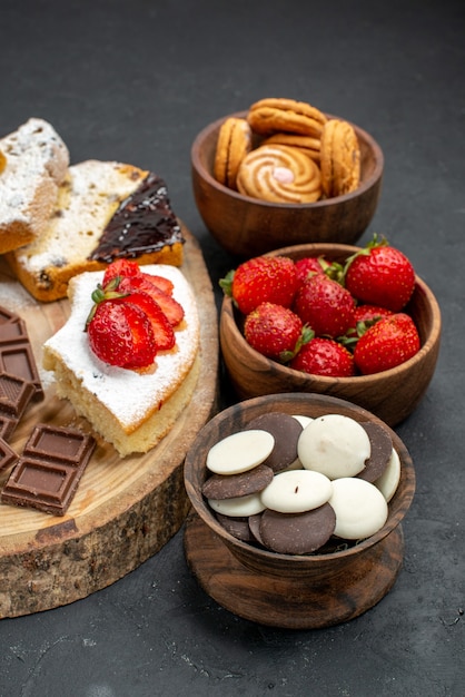 Fette di torta vista frontale con biscotti di frutta e barrette di cioccolato su sfondo scuro