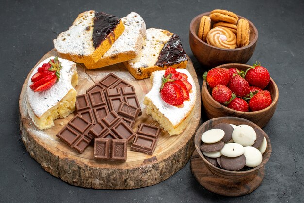 Fette di torta vista frontale con biscotti di frutta e barrette di cioccolato su sfondo scuro