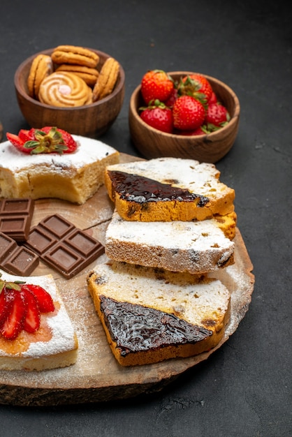 Fette di torta vista frontale con biscotti e frutta su sfondo scuro