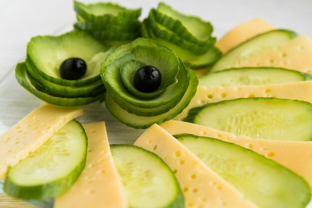 Fette fresche di formaggio, cetriolo e avocado con olive sul piatto