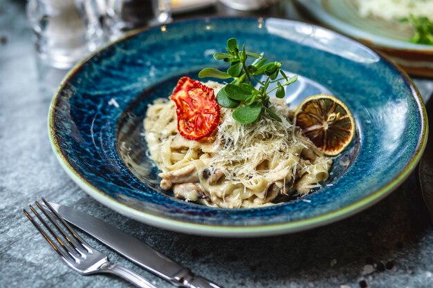 Fettuccine ai funghi cremoso vista laterale funghi sale pepe aglio formaggio e pomodoro secco su un piatto