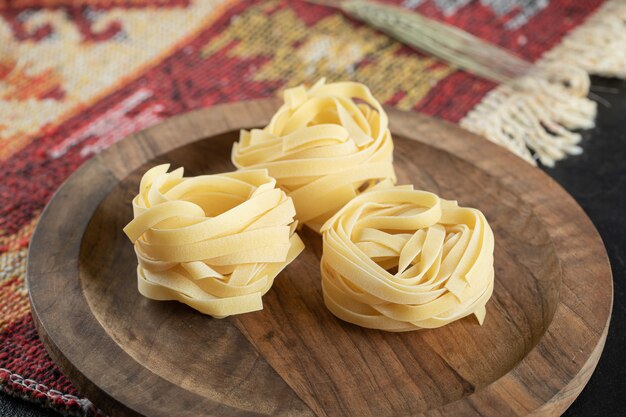 Fettuccine crude arrotolate italiane su tavola di legno con grano