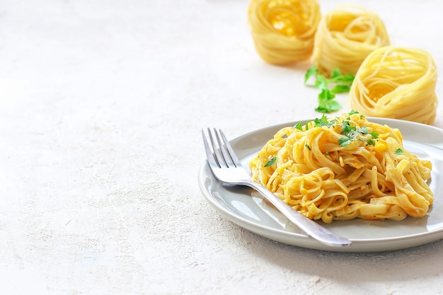 Fettucine di zucca Alfredo in un piatto di ceramica con fette di zucca crude fresche. Pasto autunnale a pranzo. Ricetta di zucca butternut.