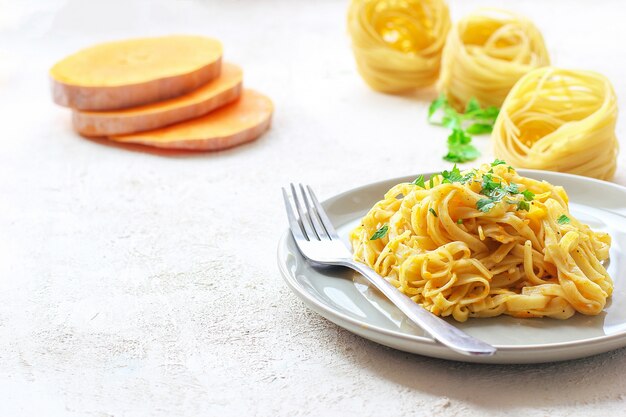 Fettucine di zucca Alfredo in un piatto di ceramica con fette di zucca crude fresche. Pasto autunnale a pranzo. Ricetta di zucca butternut.