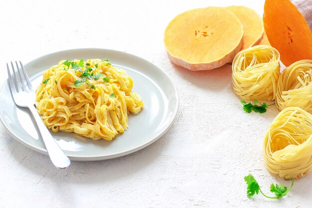 Fettucine di zucca Alfredo in un piatto di ceramica con fette di zucca crude fresche. Pasto autunnale a pranzo. Ricetta di zucca butternut.