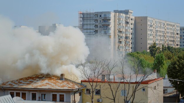 Fiamme che escono dalla casa in fiamme nel quartiere. Fumo che emerge dal tetto in fiamme nel paesaggio della città. Fumi pericolosi e smog dall'esplosione che escono dall'edificio distrutto