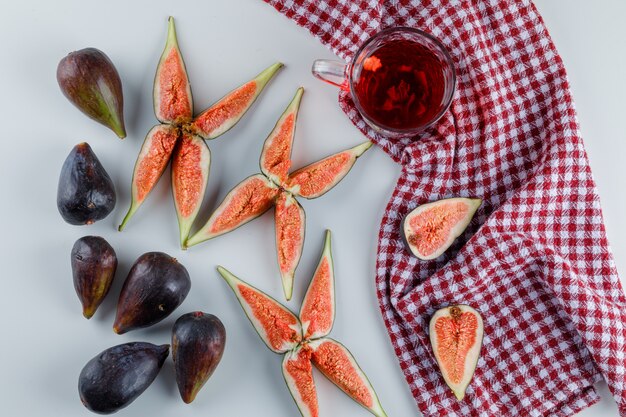 Fichi con fette, tazza di tè su bianco e asciugamano da cucina, piatto disteso.