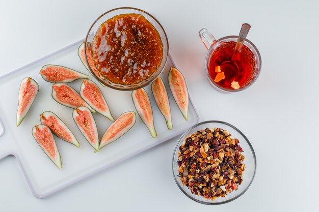 Fichi con marmellata di fichi, tè, cucchiaino, vista dall'alto di erbe secche su bianco e tagliere