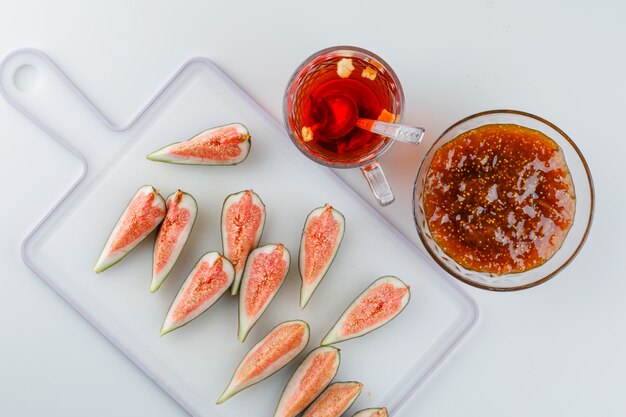 Fichi con marmellata di fichi, tisana, cucchiaino vista dall'alto su bianco e tagliere