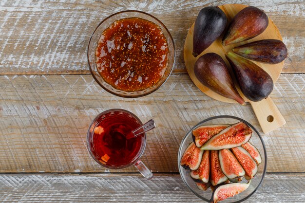 Fichi con tè, marmellata di fichi, cucchiaino in una ciotola su legno e tagliere, piatto disteso.