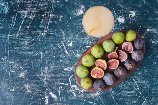 Fichi verdi con una tazza di bevanda sull'azzurro.