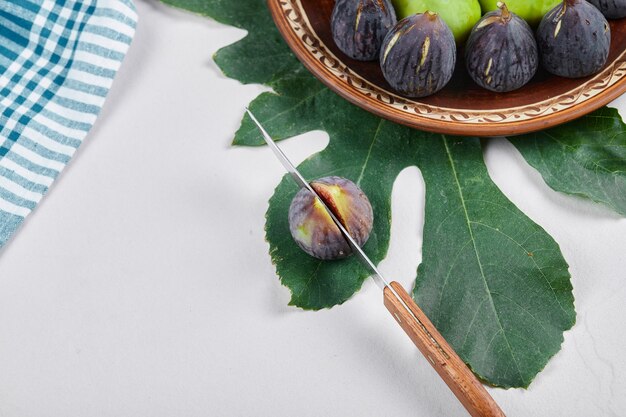 Fichi verdi e neri su un piatto di ceramica con un coltello e una foglia. Foto di alta qualità