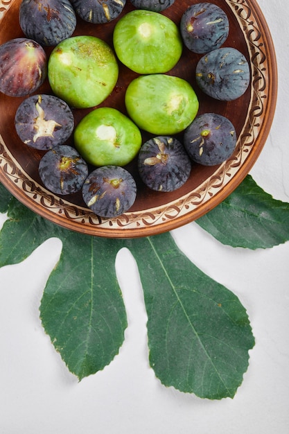 Fichi verdi e neri su un piatto di ceramica e su uno sfondo bianco. Foto di alta qualità