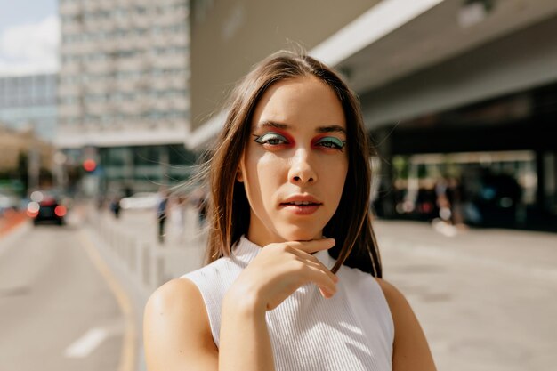 Fiduciosa bella ragazza con i capelli scuri e trucco luminoso è in posa alla macchina fotografica all'aperto alla luce del sole Signora allegra che fa selfie in una giornata di sole Bella ragazza con i capelli corti scuri