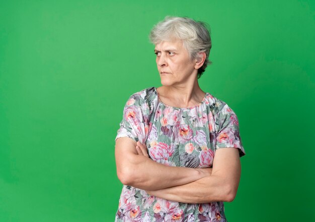 Fiduciosa donna anziana attraversa le braccia guardando il lato isolato sulla parete verde