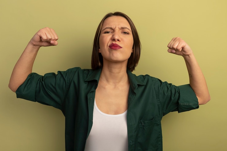 Foto gratuito fiduciosa donna graziosa tempi bicipiti isolati sulla parete verde oliva