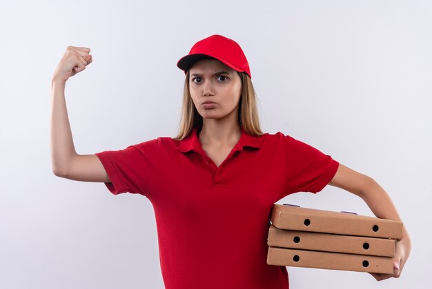 Fiduciosa giovane donna delle consegne che indossa l'uniforme rossa e cappuccio tenendo le scatole per pizza e facendo un gesto forte