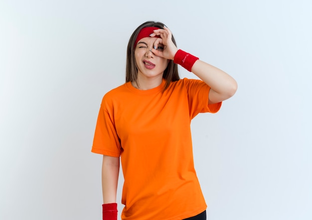 Fiduciosa giovane donna sportiva che indossa fascia e braccialetti facendo sguardo gesto sbattere le palpebre isolato sulla parete bianca con lo spazio della copia