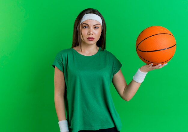 Fiduciosa giovane donna sportiva che indossa la fascia e braccialetti tenendo palla da basket cercando