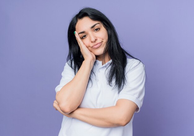 Fiduciosa giovane ragazza caucasica bruna mette la mano sul viso che sembra isolato sulla parete viola