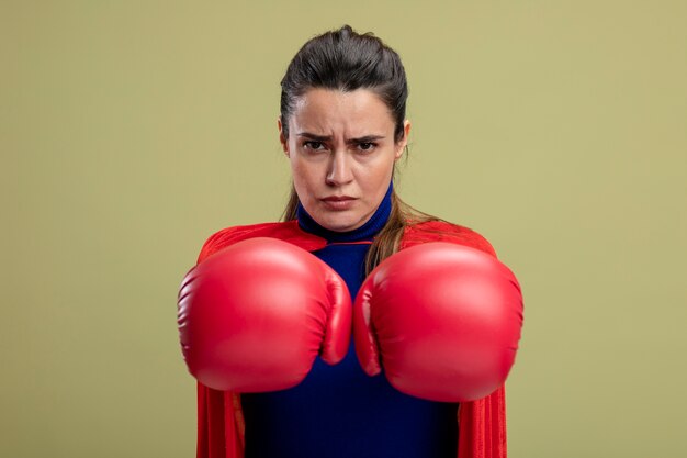 Fiduciosa giovane ragazza del supereroe che indossa guantoni da boxe tendendo le mani alla telecamera isolata su sfondo verde oliva