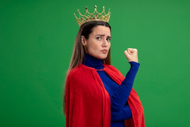 Fiduciosa giovane ragazza del supereroe che indossa la corona che mostra un forte gesto isolato su sfondo verde