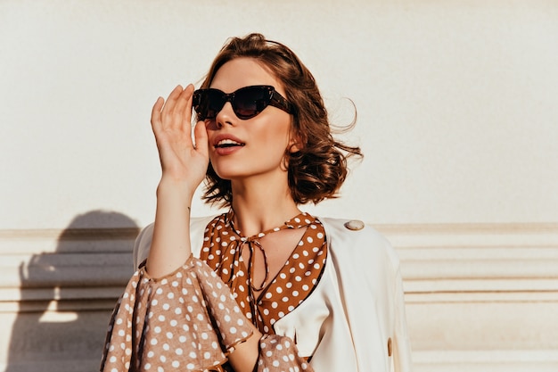 Fiduciosa ragazza caucasica in occhiali da sole scuri guardando in lontananza. Colpo esterno di donna alla moda di buon umore.