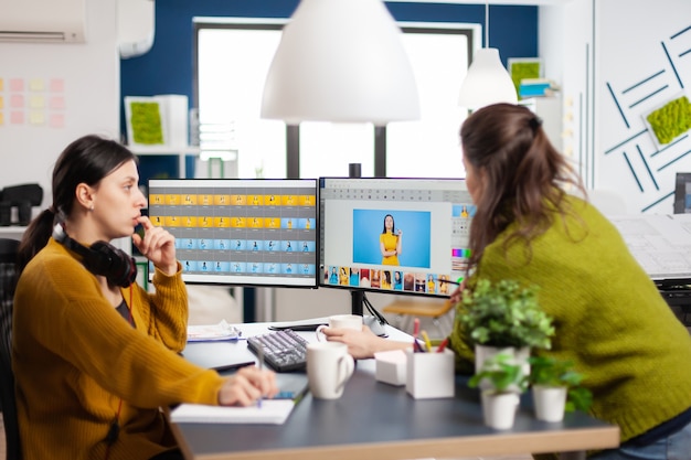 Fiduciose donne editor di foto seduti al posto di lavoro in studio creativo ritocco foto, art director che spiega la tecnica di greding del colore