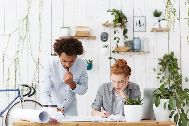 Fiduciosi architetti o ingegneri dalla carnagione scura, uomini e donne dai capelli rossi, brainstorming