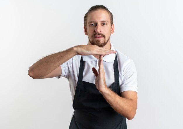 Fiducioso giovane barbiere bello che indossa l'uniforme facendo gesto di timeout isolato su bianco con lo spazio della copia