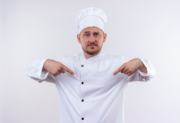 Fiducioso giovane bel cuoco in uniforme da chef che punta a se stesso isolato su muro bianco