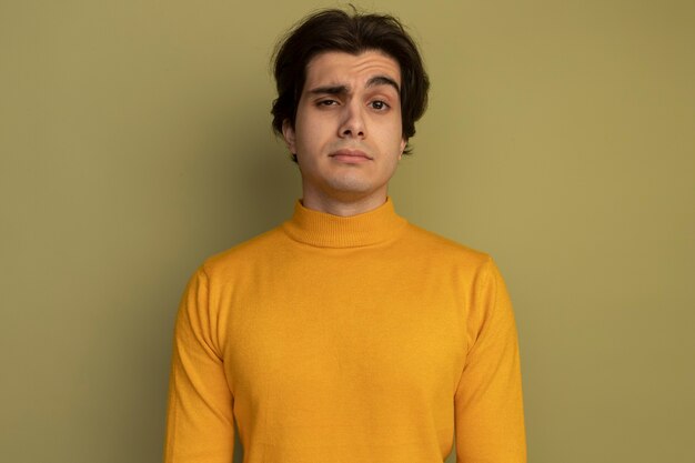 Fiducioso giovane bel ragazzo indossa maglione dolcevita giallo isolato sulla parete verde oliva