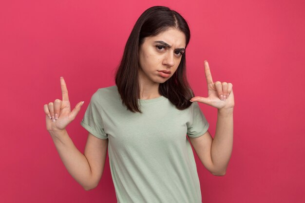 Fiducioso giovane bella ragazza caucasica che fa il gesto della pistola isolata sulla parete rosa