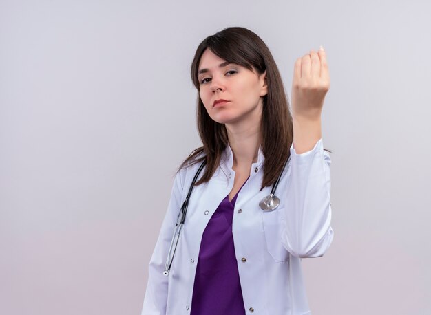Fiducioso giovane dottoressa in abito medico con lo stetoscopio tiene la mano su sfondo bianco isolato con spazio di copia