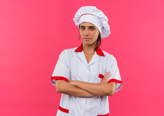 Fiducioso giovane femmina cuoco indossando chef uniforme incrocio mani sulla parete rosa isolata con lo spazio della copia