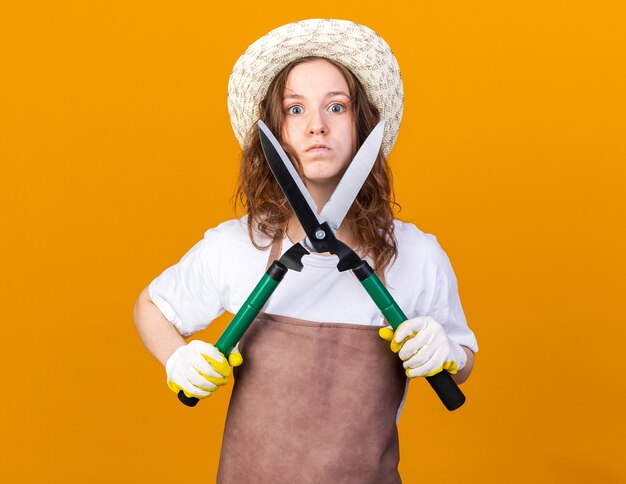 Fiducioso giovane giardiniere femminile che indossa cappello da giardinaggio con guanti che tengono cesoie da potatura