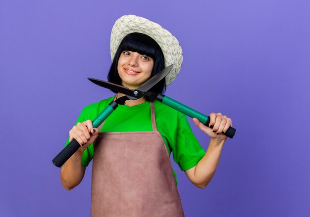 Fiducioso giovane giardiniere femminile in uniforme che indossa un cappello da giardinaggio tiene le forbici