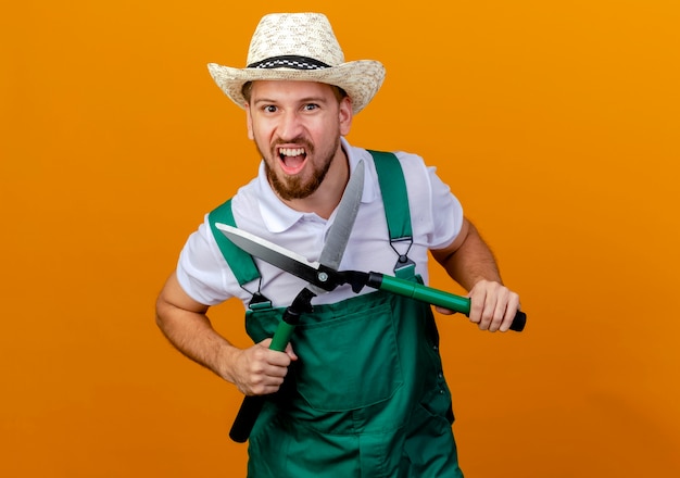 Fiducioso giovane giardiniere slavo bello in uniforme e cappello che tengono i potatori che sembrano isolati