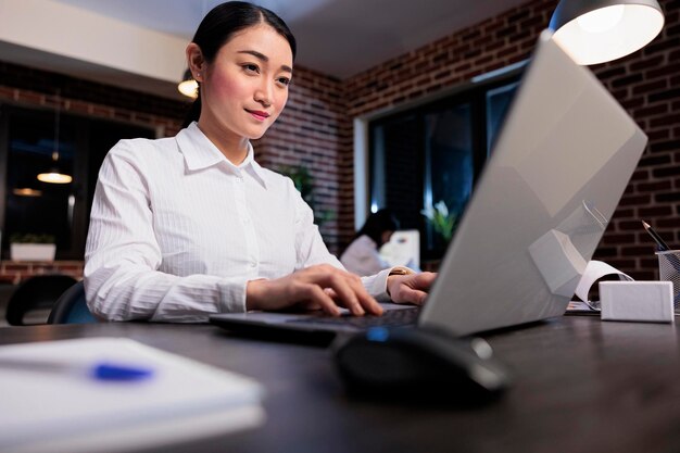 Fiducioso giovane imprenditore adulto che lavora al computer portatile mentre sviluppa la strategia di marketing. Felice positivo dipendente della società di affari seduto alla scrivania nell'area di lavoro dell'ufficio durante l'analisi del piano di gestione.