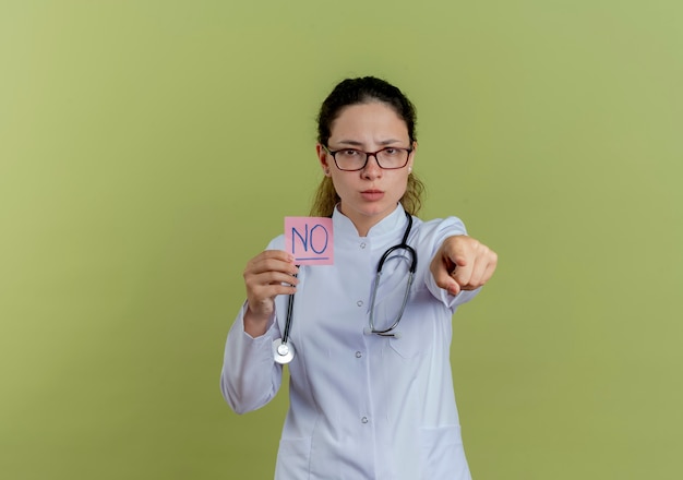 Fiducioso giovane medico femminile che indossa abito medico e stetoscopio con gli occhiali in possesso di punti di carta nota isolati