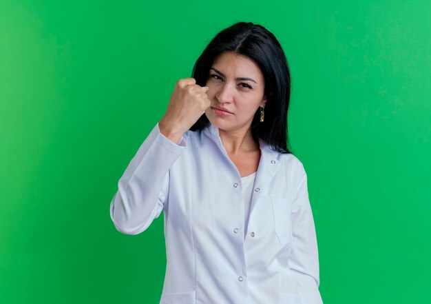 Fiducioso giovane medico femminile che indossa abito medico facendo essere forte gesto isolato sulla parete verde con copia spazio