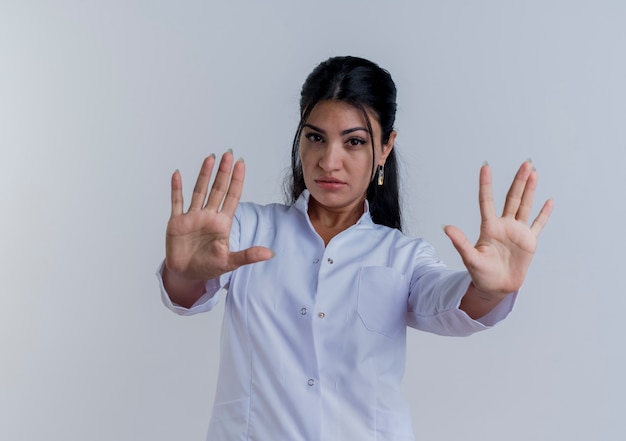 Fiducioso giovane medico femminile che indossa abito medico guardando facendo gesto di arresto isolato