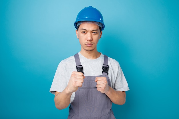 Fiducioso giovane operaio edile che indossa il casco di sicurezza e uniforme facendo gesto di boxe