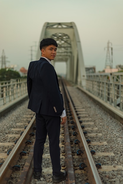 Fiducioso giovane uomo asiatico in un vestito in piedi nel mezzo di una ferrovia guardando indietro