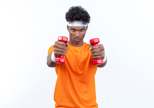Fiducioso giovane uomo sportivo afro-americano che indossa la fascia e il braccialetto tenendo fuori i manubri
