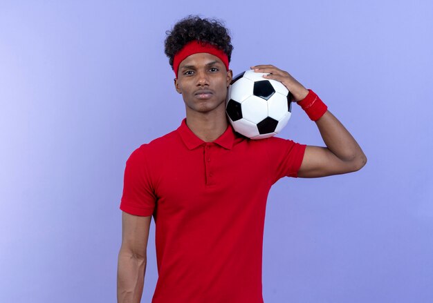 fiducioso giovane uomo sportivo afro-americano che indossa la fascia e il braccialetto tenendo palla sulla spalla