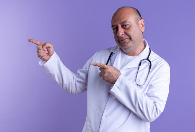 Fiducioso maschio di mezza età medico indossando accappatoio medico e uno stetoscopio guardando davanti rivolto verso il lato isolato su viola wall