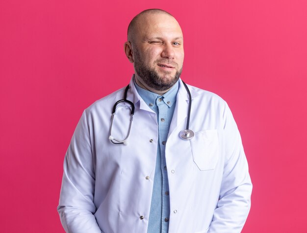 Fiducioso medico maschio di mezza età che indossa una tunica medica e uno stetoscopio che fa l'occhiolino