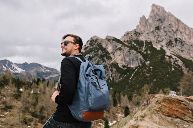 Fiducioso uomo soddisfatto con il sorriso che guarda nel cielo godendo l'aria fresca di montagna durante il viaggio