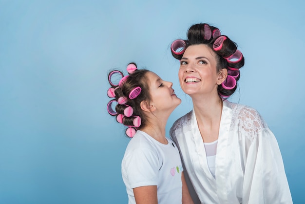 Figlia che bacia la madre in bigodini e accappatoio